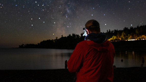 Hayes stands in the dark with his camera while the stars above shine brightly by Lake Superior. 