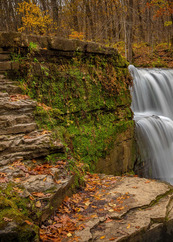 Next to a waterfall is a rocky outcrop and steps covered with green moss. 