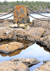 A rocky outcrop along Lake Superior and a stone railing are covered in bright orange lichen.