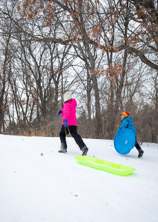 Two children run up a snowy hill with sleds. 