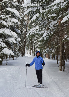 A person on skis smiles at the camera surrounded by pine trees. 