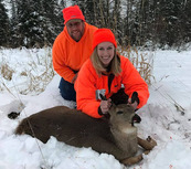 hunter in blaze orange with deer she harvested and man in blaze behind her