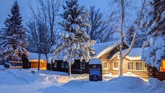 A snow-covered inn is illuminated by warm yellow light. 