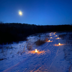 A snowy path is illumined by candles along the trail in winter. 