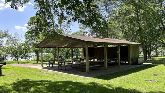 A picnic shelter with many tables underneath on a bright summer day. 