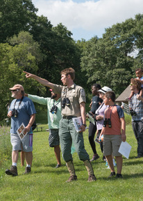 A naturalist leads a group of people through a prairie, pointing out plants and animals as they go. 