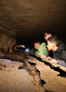 A group of teens look at cave formations with a flashlight. 