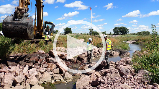 Photo show stream with rock, and workers doing restoration project