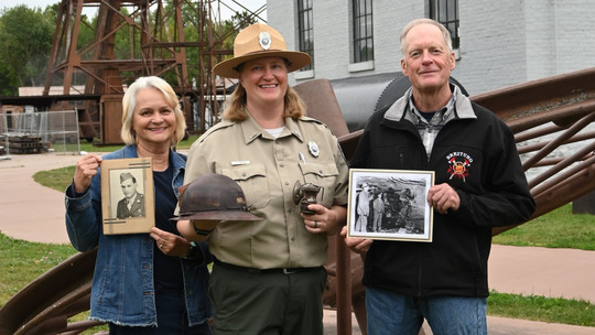 Park ranger Jody stands in uniform between her parents. Her parents hold up photos of the grandparents who also worked in the park. 