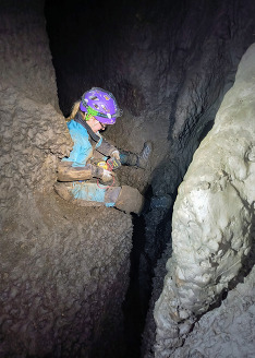 A researcher sits on the ground of a dark cave while looking at a clip board. 