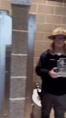 Jody holds a plaque for America's Best Restroom at Bear Head Lake State Park. She holds it up to the state park entrance sign as if to hang it. 