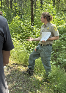 A naturalist intern holds a paper up while giving a presentation outside.
