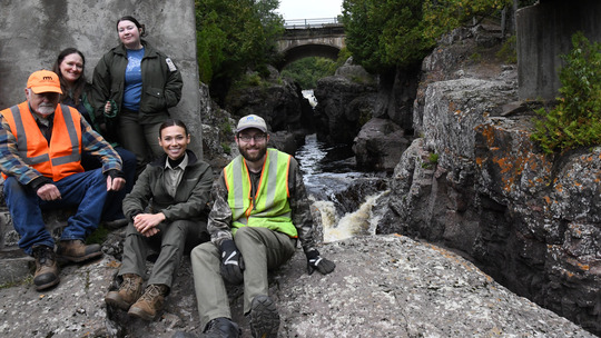 A group of park workers pose smiling at the camera from an outcropping of rocks next to a river. 