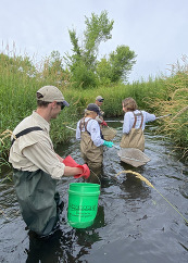 A group of interns wade in a waterway using nets.