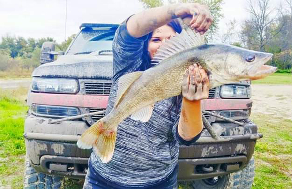 woman holding walleye and top fin up standing in front of pickup truck