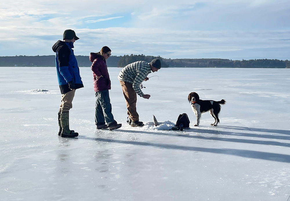 family and dog on the ice with angler pulling a fish up