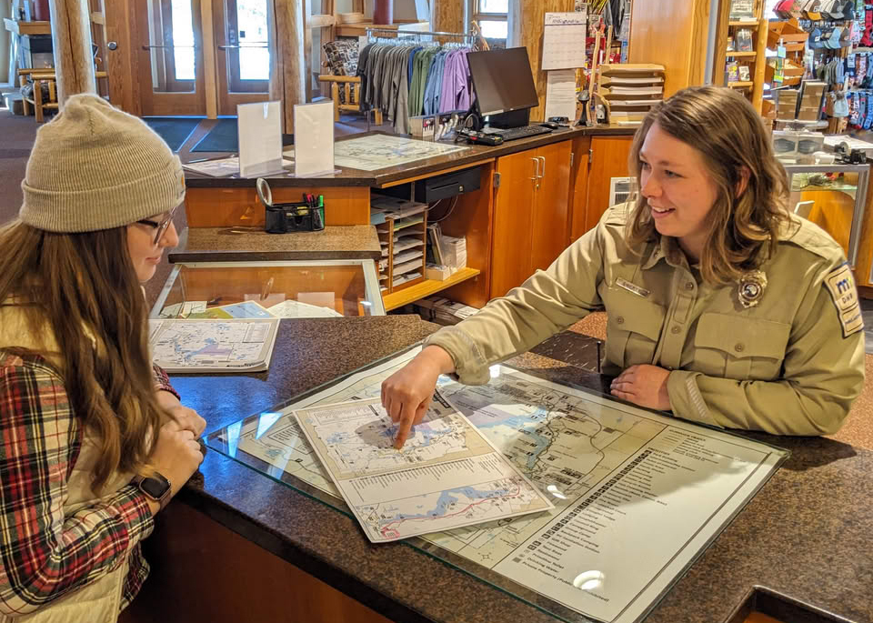 A park worker smiles while pointing out a feature on a map.