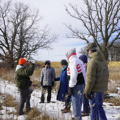 A group of people pay attention to a naturalist in a snowy prairie.