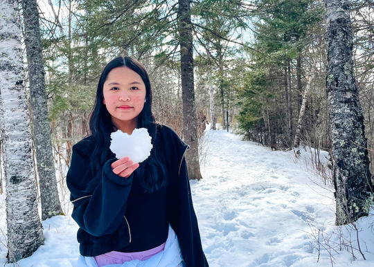 A young woman with a slight smile holds up a snow heart.
