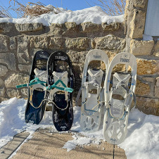 Two sets of snowshoes lean against a stone wall.