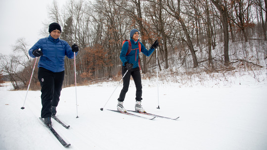 Two people ski along a smooth, snowy path.