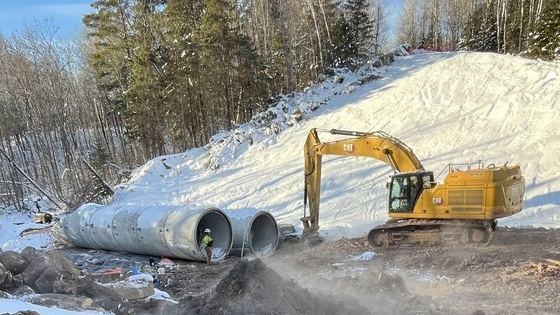 Large construction equipment next to culvert pipes. 