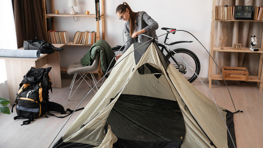 A person sets up a tent and packs for a camping trip while in their home.