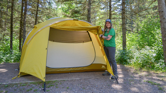 An I Can! instructor holds the flap of a tent open while smiling. 