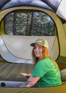 Anna sits in a tent with her hand on an air mattress smiling. 