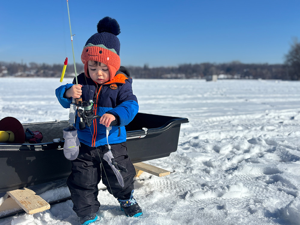 young angler out ice fishing near a sled that's modified to slide on skis