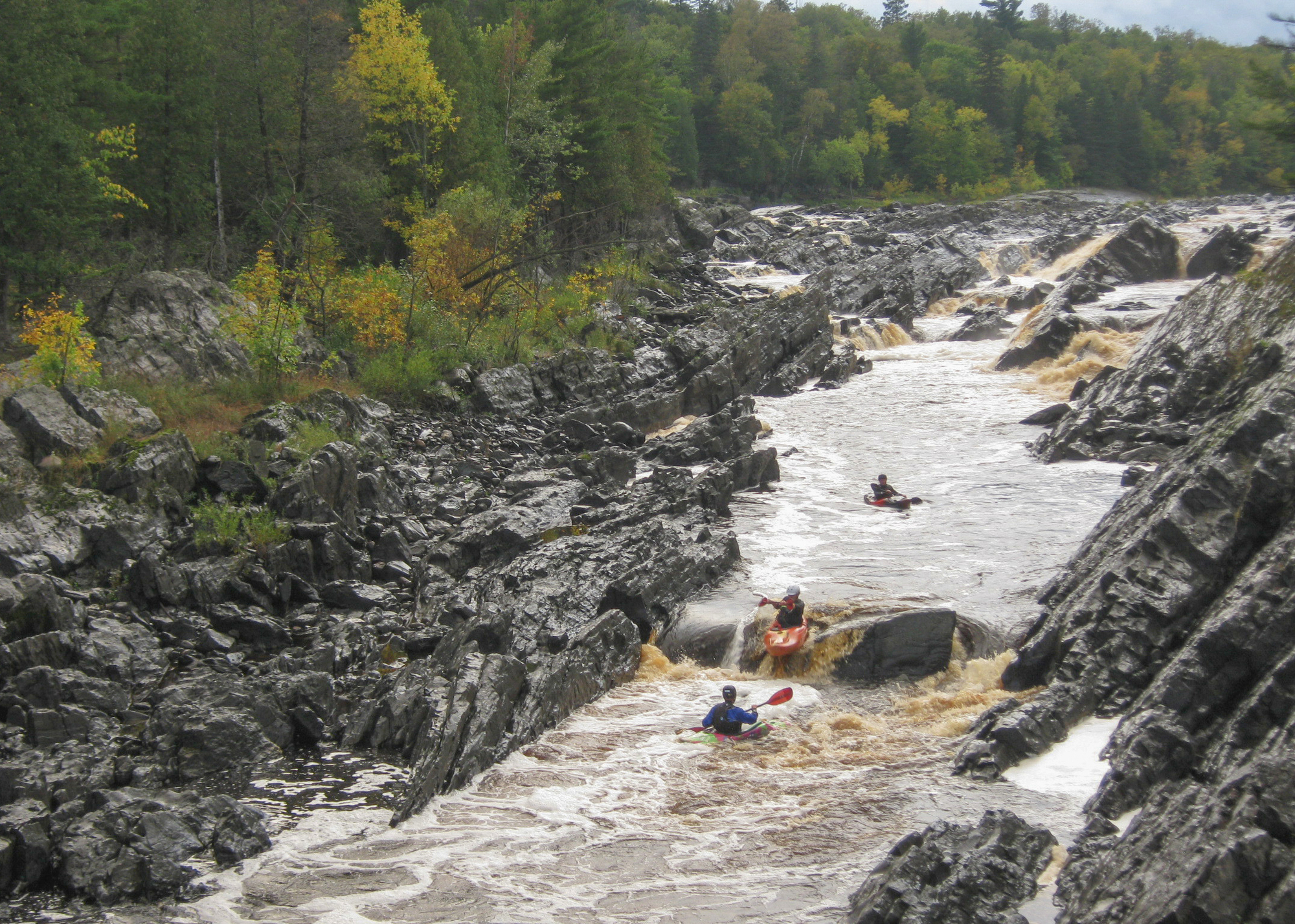 A group of kayakers paddle down rapids on a Minnesota river.