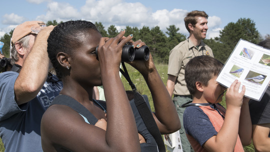 A group of people look through binoculars on a sunny day.