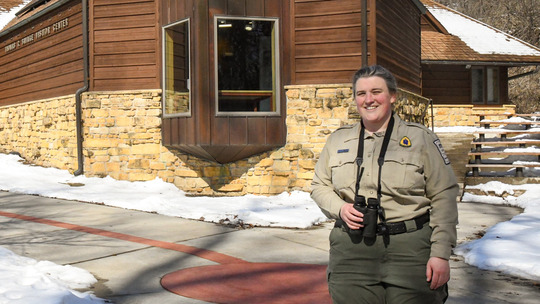 Amy Mester, naturalist, stands with binoculars in front of the Fort Snelling State Park visitor center.