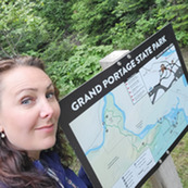 Amy smiles in front of the Grand Portage State Park map on a sign.