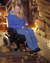 A young woman in a wheelchair looks through the steel grate flooring on a cave tour. 