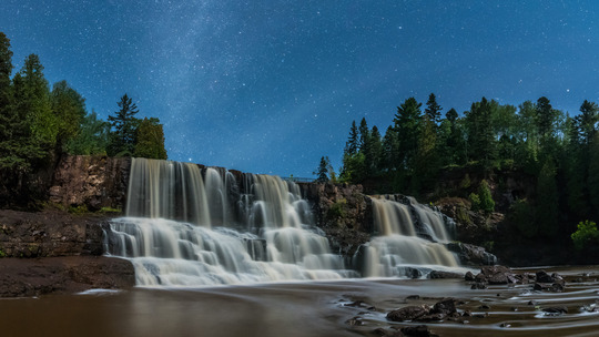 Gooseberry Falls waterfalls flow gently at night with stars and the Milky Way overhead.