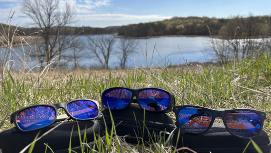 Three sets of glasses with blue-tinted lenses sit outside with a lake view behind them.