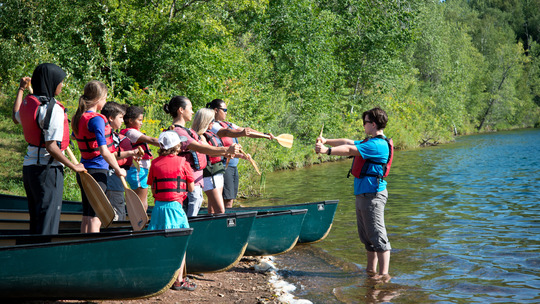 A group of young adults watch an instructor demonstrate how to paddle.