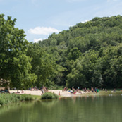 Across a lake, a beach is covered in visitors lounging and swimming. 