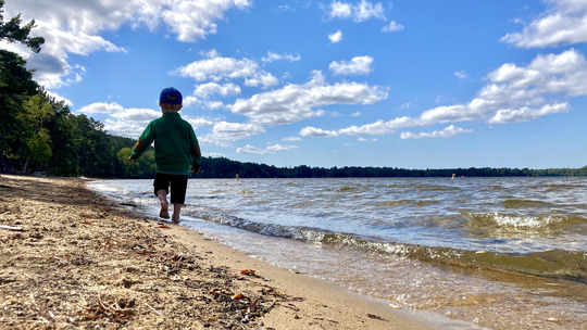 A young child walks along a beach on a sunny day.
