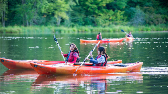 A parent and child kayak along a river while chatting with one another. 