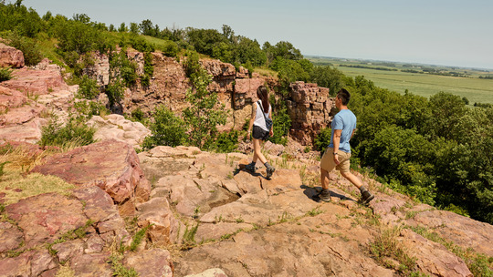 Two people walk along the edge of a red cliff.