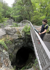 A person reads a sign next to a railing above a deep, cavernous hole in the ground. 
