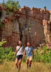 Two people look up with admiration at the tall rock outcrop behind them.