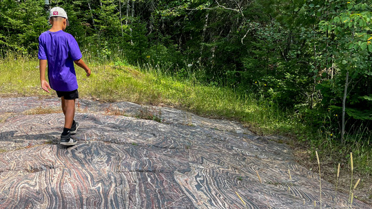 A teen walks along a flat outcrop of black and red striped rock.
