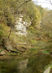 A limestone outcrop hovers over a shallow stream. 