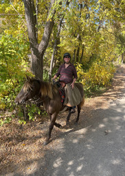 A rider smiles on horseback surrounded by bright yellow fall foliage.