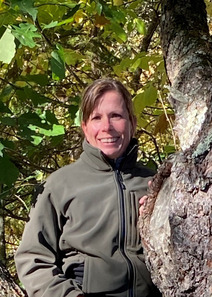 Sandra smiles at the camera while standing next to an oak tree. 