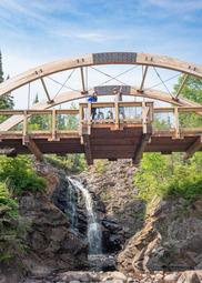 An arching bridge extends over a rocky waterfall. 