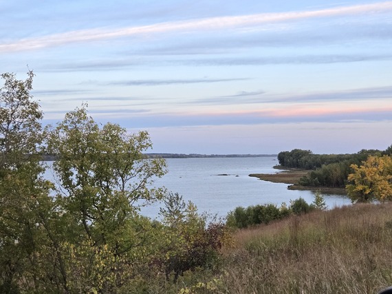 Sunrise over a calm lake with cotton candy sky and fall foliage along the shoreline. 